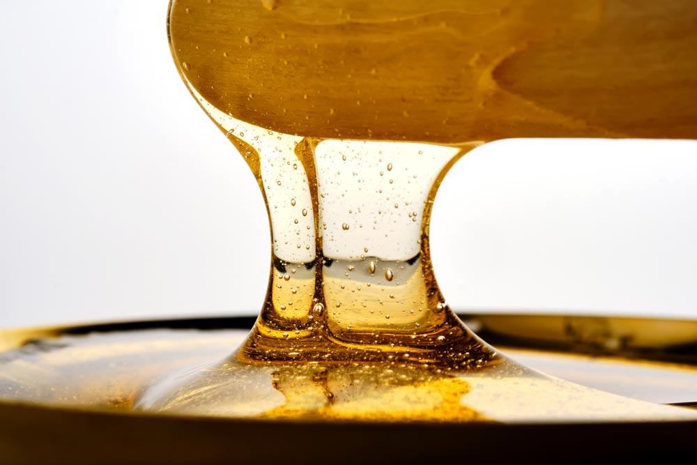 En dramatisk närbild av gyllene vax som rinner från en träslev i två tjocka, läckra strålar